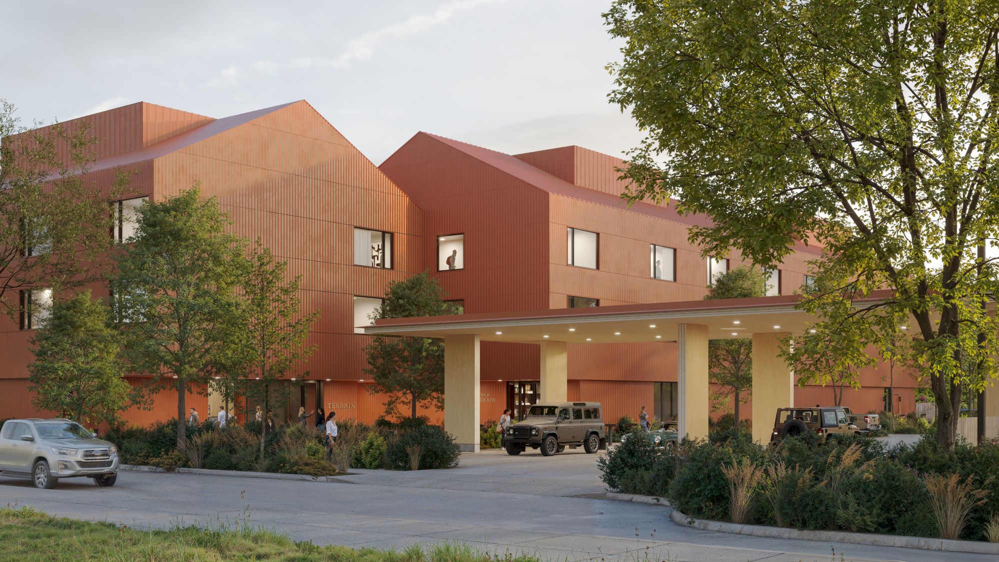 The image shows a modern brick building with a covered entrance, surrounded by trees and parked cars in the foreground.